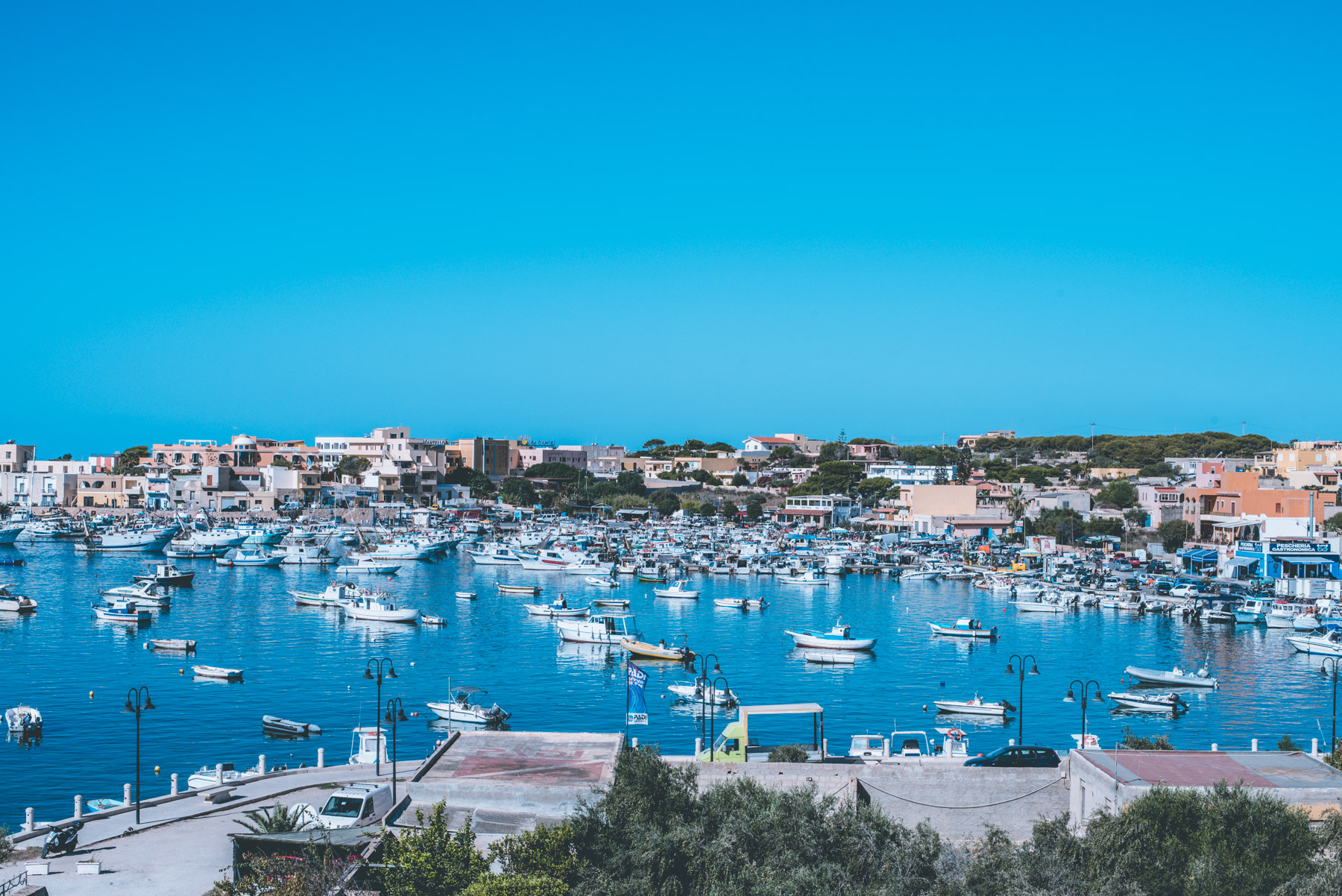 a panoramic view of the harbour of lampedusa with houses blue sea and white boats