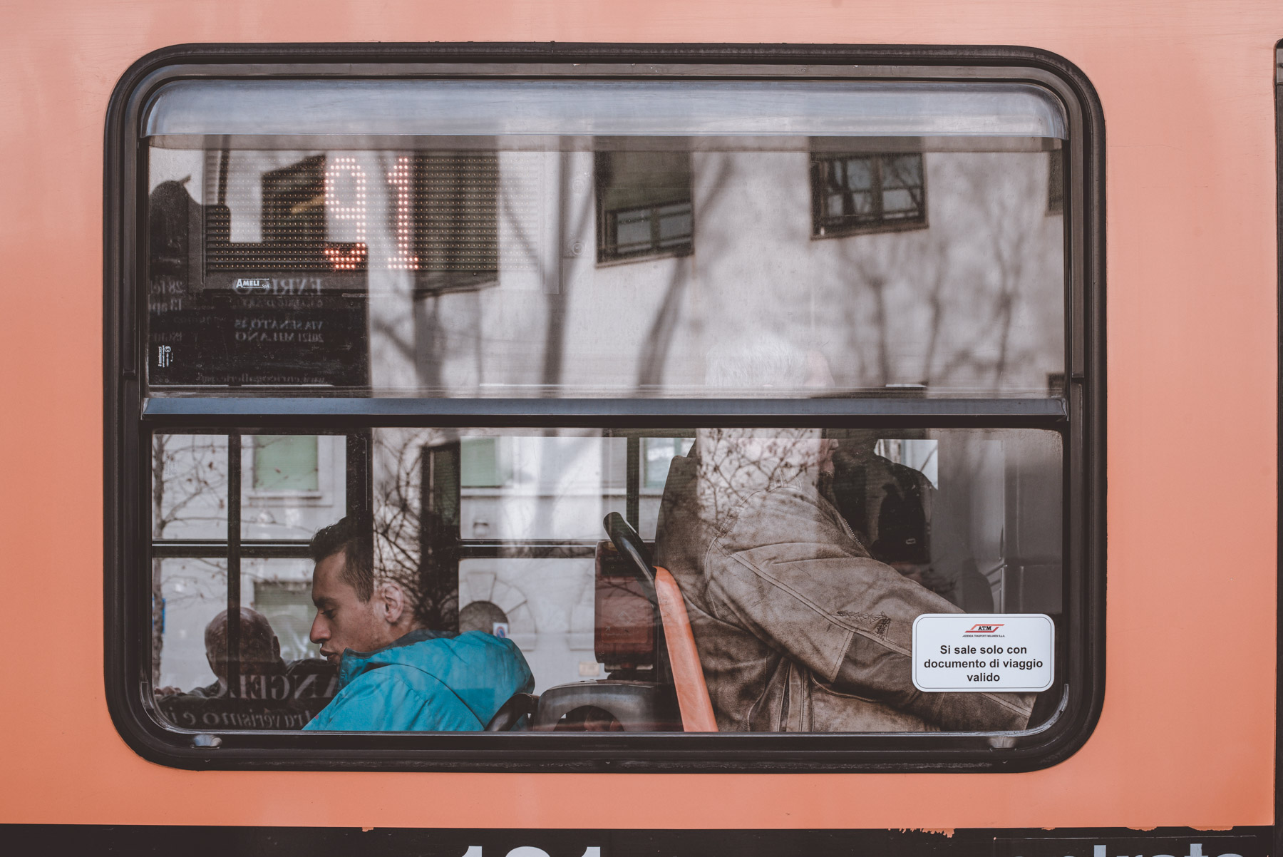 a street photograph showing some reflections and some people on the bus in the city of Milan