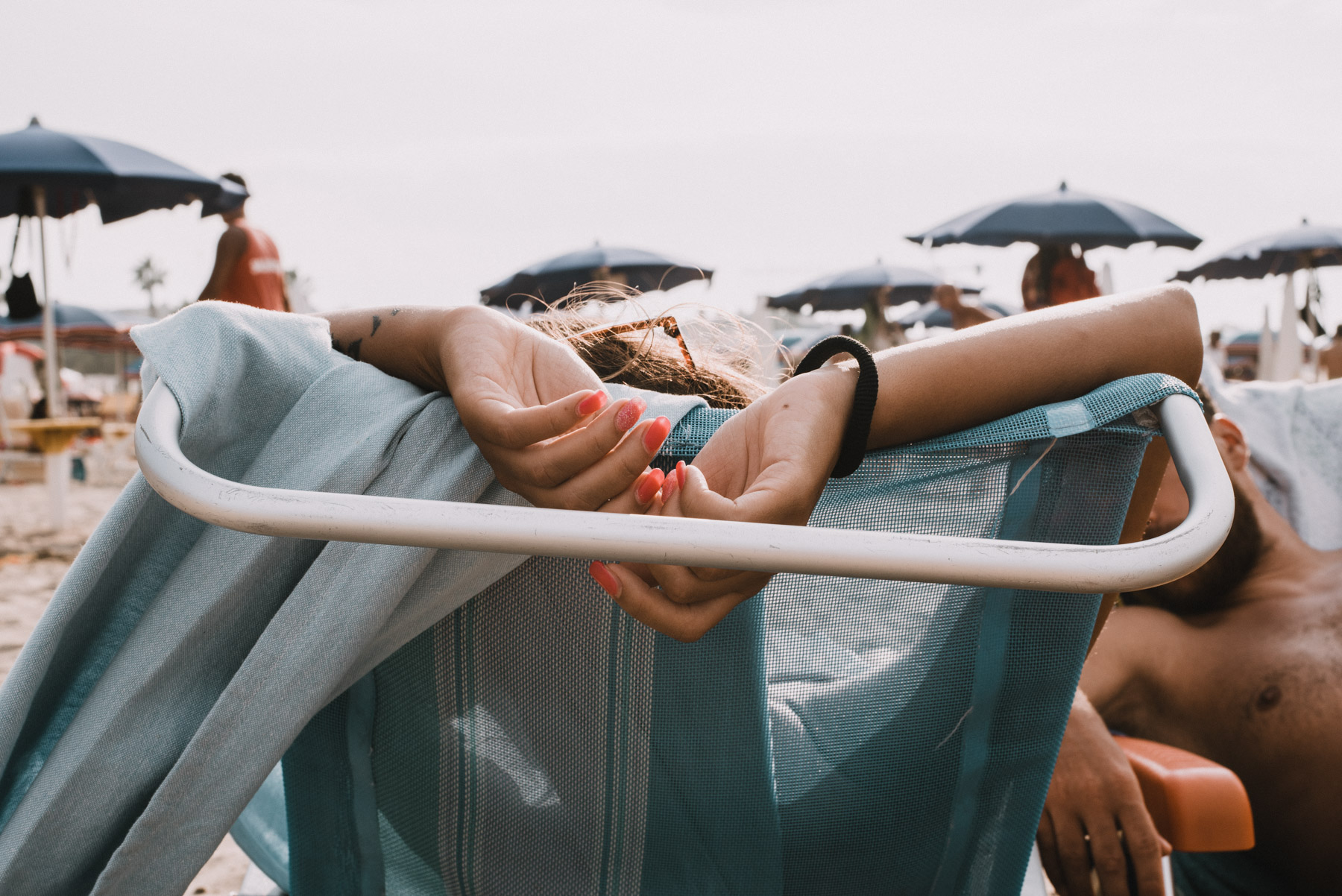dettaglio delle mani con smalto di una ragazza che si rilassa al mare in spiaggia a Barletta in Puglia, detail of pink nails of a girl having some relaxing time on the beach by the sea in the city of Barletta in Apulia
