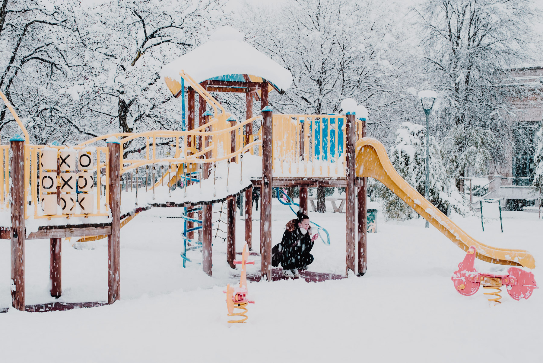 Snow in Milan on December 2020, a girl shields from the snow below the play area in a park, nevicata a Milano il 28 dicembre 2020, una ragazza cerca riparo dalla neve sotto lo scivolo dell'area giochi per bambini al parco Formentano presso Largo Marinai d'Italia
